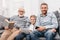Father, son and grandfather relaxing together on couch in living room with digital tablet, smartphone