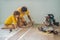 Father and son installing new wooden laminate flooring on a warm film floor. Infrared floor heating system under