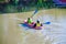 Father and son in kayak boat on pond with father watching boy row from behind - reflections and moored boats in background - the