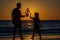 Father and son playing with toy ship on sea beach at the summer sunset. Concept of friendly family. Sunset silhouette of