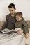 Father and son reading a book on the bed at home. Young attractive man and little boy resting in bedroom. Natural earth