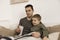 Father and son reading a book on the bed at home. Young attractive man and little boy resting in bedroom. Natural earth