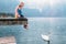 Father with son sit on wooden pier and look on white swan swims