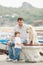 Father and son sits with dogs on a bench near the sea