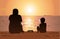 Father and son sitting on the beach, watching sunset