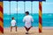 Father and son talking on swings on the beach