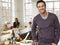 Father Standing At Kitchen Counter While Family Sitting In Background