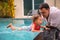 Father teaches cute toddler little girl in swimsuit to swim in the pool holding his hand