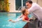 Father teaches cute toddler little girl in swimsuit to swim in the pool holding his hand