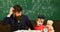 Father teaches son, discuss, explain. Teacher in formal wear and pupil in mortarboard in classroom, chalkboard on