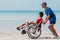 Fatherâ€‹ and Asian special child on wheelchair playing, doing activity on  sea beach in summer,