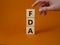 FDA - Food Drug Administration symbol. Wooden cubes with word FDA. Doctor hand. Beautiful orange background. Medical and Food Drug