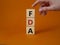 FDA - Food Drug Administration symbol. Wooden cubes with word FDA. Doctor hand. Beautiful orange background. Medical and Food Drug