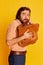 Fear. Portrait of bearded hairy man, shy scientist nerd in flared jeans standing with briefcase over yellow background