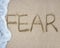 Fear word hand written with wave foam on sand beach