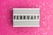 February text on white lightbox. Pink background with multicolored confetti. Flat lay style. Top view