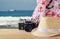 Fedora hat, old vintage camera and scarf over wooden table and sea landscape background. relaxation or vacation concept