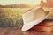 Fedora hat and stack of books over wooden table and field of wheat country side background. relaxation or vacation concept