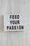 `Feed your passion` words on a lightbox on a white wooden background, top view. Overhead, from above, flat lay. Close-up