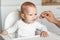 Feeding of cute baby with a spoon in the kitchen