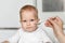 Feeding of cute baby with a spoon in the kitchen