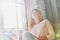 Feeling calm and happy. Attractive young woman keeping eyes closed and smiling while sitting on the window sill at home