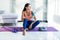 Feeling thirsty. Tired young woman in sports clothing drinking water while sitting on the exercise mat at home