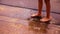 Feet of a barefoot child stand in a puddle during golden hour as gentle raindrops fall