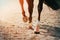 The feet of a black racehorse galloping across a sandy arena