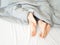 Feet of couple sleeping side by side in comfortable bed. Close up of feet in a bed under white blanket. Bare feet of a
