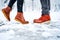 Feet of a couple on a snowy sidewalk in brown boots