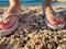Feet Girl with a neat pedicure in women`s stylish beach flip-flops aqua on the beach background. Two sandals on the sand near the