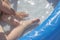 Feet and hand of a child bathing in a blue plastic pool. Little kid plays in a transparent pool with dandelions. Water procedures