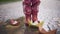Feet of little girl in rubber boots stomping in puddle with paper boats around. Unrecognizable happy kid having fun