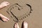 Feet of man and woman standing on the beacht with heart drawn on the sand