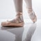 Feet with pink satin pointe shoes of a classical dancer posing and reflected on the polished floor