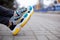 Feet shod in sneakers multi-colored yellow, white, black and blue are on the asphalt road.