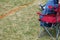 Feet in sneakers of supporter or fan of sports competition team sitting in outdoor camping chair on the edge of football