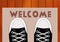 Feet teen in sneakers close up on a doorway rug that says Welcome in front of the house.