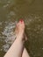 Feet of a white girl with a pedicure and painted bright pink nails in the water