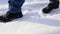 Feet of a woman walking in the snow on a snowy day in black boots and blue jeans. Side view. Walk in the snowy city.