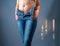 Female abdomen with postpartum stretch marks. Blue jeans are torn on her bare belly. Hands on hips