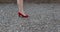 Female adult legs wearing elegant red high-heeled shoes on the feet, walking on a stony path