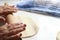 Female aged hands with a wooden rolling pin shaping a kneaded dough dusted with flour in kitchen