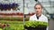 Female agricultural engineer walking with box full of seedling in greenhouse medium close-up