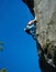 Female alpinist climbing mountain under blue sky.