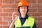 Female architect or builder holding a clipboard and giving the ok sign on brick wall background