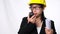 Female architect in a helmet holding construction plans and using walkie-talkie and talk to other staff on a white background in s