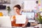 Female Architect In Office Making Video Call At Desk On Laptop And Showing Building Plans