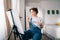 female artist sitting in front of easel, painting picture with inspiration, drawing on canvas with paintbrush, palette